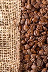 Rustic coffee beans spilled over textured burlap napkin background