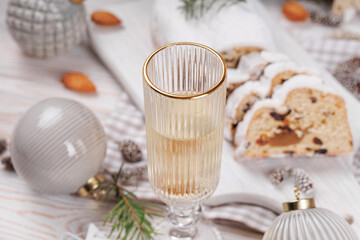A holiday celebration setting featuring a champagne glass filled with sparkling wine, Christmas ornaments, and slices of traditional stollen cake on a beautifully decorated table.