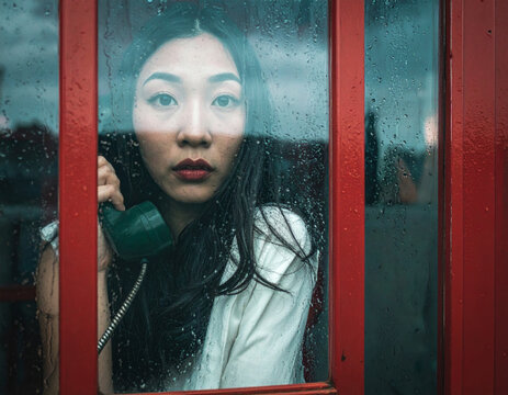 Mujer en apuros asustada llamando a emergencias desde una cabina telef&oacute;nica.
