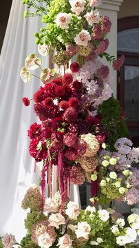 Colorful wedding romantic flower arch with white fabric. Summer atmosphere on the street. Green white and red flowers. Rose, hydrangea, anthurium, dahlia, chrysanthemum, amaranth, dianthus white spray