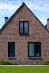 Obraz premium Modern brick house with large windows set against a clear sky, featuring a well-manicured lawn and fresh green landscaping in an attractive neighborhood