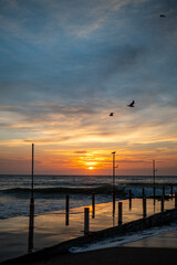 Seaside pier at sunrise with flying birds over ocean waves. Vertical landscape photography with copy space. Summer travel and vacation concept