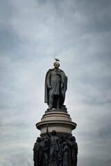 Fototapeta premium Ominous statue of a historical figure stands tall against a moody, cloudy sky, with a lone bird perched atop.