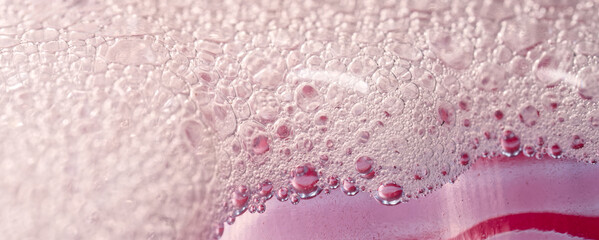 Close-up macro shot of pink foamy cleaning liquid with sparkling bubbles on a red surface, creating a delicate and abstract texture. Photo