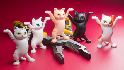 Cute toy cats with raised paws stand around pliers on a red background, symbolizing a friendly team of builders or electricians at work. Photo