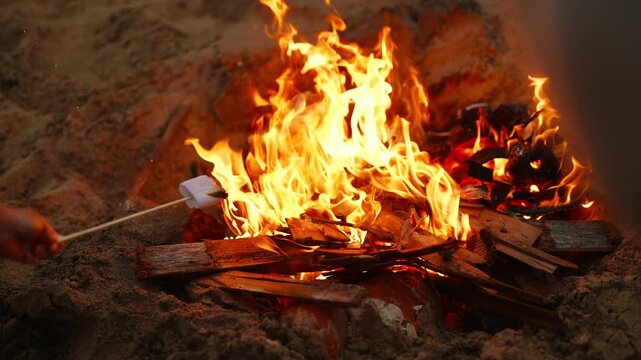 A fire is burning in a pit, with marshmallows being toasted over it. The fire is hot and bright, and the marshmallows are being cooked to a golden brown. The scene is cozy and inviting