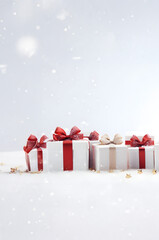 Large horizontal row of Christmas gifts with red ribbons and spruce trees on snow covered surface, snowfall and abstract background with snowflakes and sparkling lights.