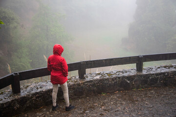 Woman in red raincoat contemplates foggy mountain view, perfect for travel, adventure, or...