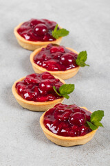 Round Cherry tartlets. With custard and mint. Light gray background.