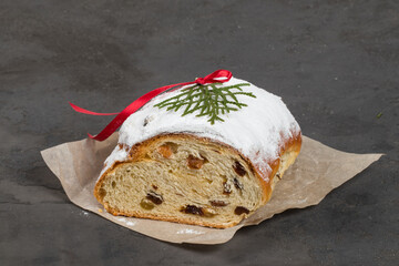 German Stollen. German Christmas cake with of spices, raisins, candied fruits, and almond cream. Sprinkled with powdered sugar. Decorated with a red satin ribbon. Dark background. Close up	
