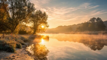 Soft light breaks through trees as the sun rises over a serene river on a foggy morning.