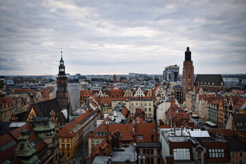 Fototapeta premium Sweeping aerial view of the historic cityscape of Wroclaw, Poland, with its iconic red-roofed buildings, ornate church spires, and modern high-rises on a cloudy day.