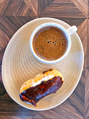 Cup of coffee and eclair on wooden table. Top view