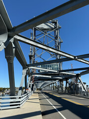 Modern lift bridge, steel truss drawbridge with metal beams, pedestrian walkway, and vehicle lanes extending over calm river