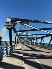 Steel truss structure of Memorial Bridge in Portsmouth, New Hampshire with pedestrian walkway and roadway under clear blue sky crossing Piscataqua River on sunny day