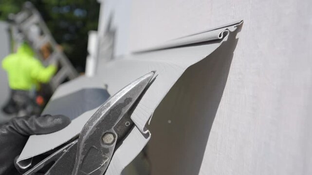 Worker cuts plastic panel for the siding renewal on outside wall of the house against bright blue sky