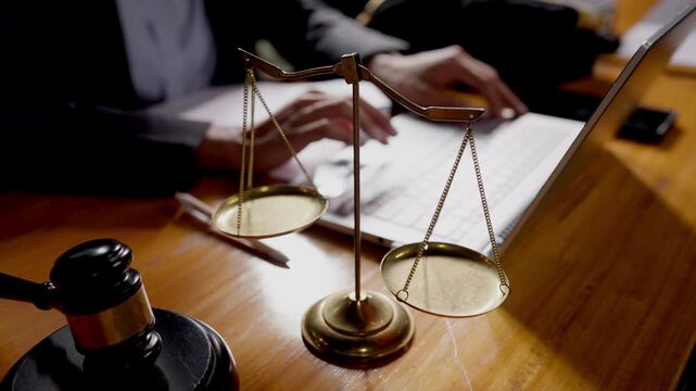 Close-up of justice scale and gavel with lawyer typing on laptop, symbol of modern legal work.