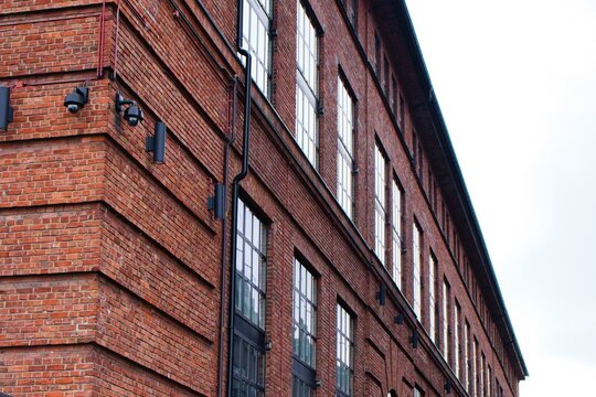 Weathered brick facade of a historic 10 building with rows of large windows and security lights, exuding a sense of timeless urban decay.