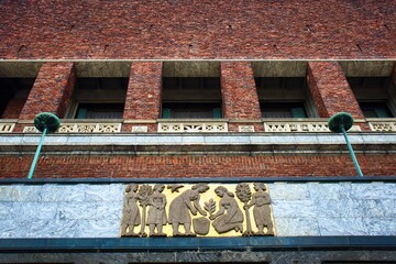 Ornate, historic brick building with intricate architectural details and a bas-relief sculpture depicting figures in an outdoor scene.