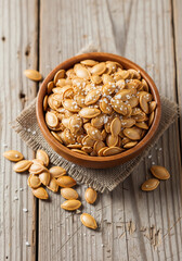 Tasty roasted pumpkin seeds seasoned with sea salt in a rustic ceramic bowl on a wooden table. Perfect healthy snack concept for autumn, organic food, and clean eating themes.
