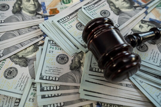 Wooden judge gavel lying on hundred dollar banknotes representing corruption, bribery and justice