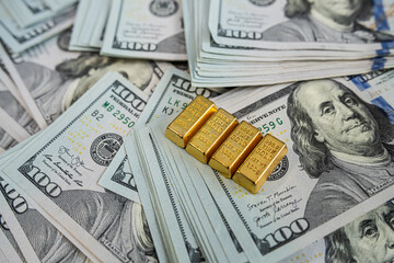 Shiny gold bullion bars on hundred dollar banknotes representing luxury, savings and financial...