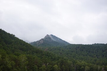 Mysterious, misty mountain peak rises above a lush, evergreen forest in a remote, picturesque landscape.