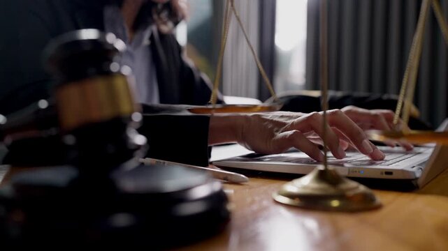 Legal scale and gavel in foreground with lawyer typing on laptop, symbolizing legal technology.