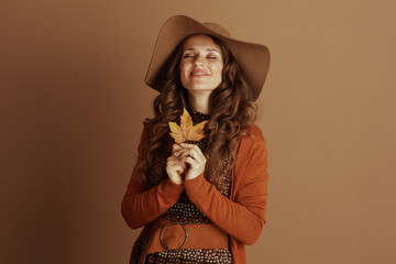 With closed eyes and a peaceful smile, a woman in a wide-brimmed hat and orange cardigan gently...