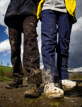 Two people standing outdoors with muddy shoes and dirty pants after hiking on a wet trail. Adventure, travel, and nature concept showing authentic outdoor experience and active lifestyle.