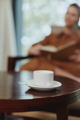 Cozy coffee break with a woman reading a book in a warm hued interior setting, featuring a cup of coffee on a wooden table