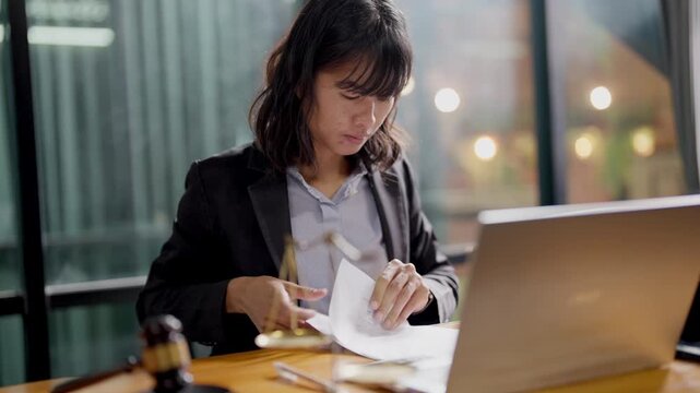 Justice gavel and scale on wooden desk with blurred hands working on laptop in background.