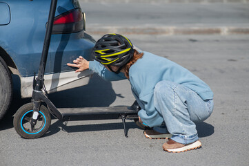 A distressed woman examines the damage after a collision between an electric scooter and a car. © Михаил Решетников
