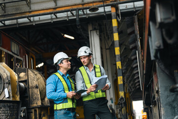 Engineers wearing safety helmets inspecting railway blueprint beside a vintage locomotive, symbolizing teamwork, innovation, and development in modern rail transportation and infrastructure projects