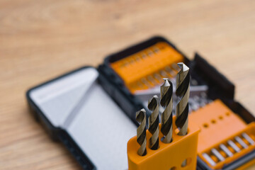 Close-up of a metal drill bit set organized in plastic case on wooden table. Concept of tools, construction, repair and DIY work.