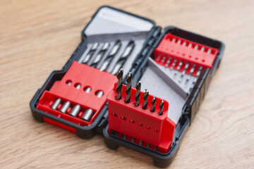 Close-up of a metal drill bit set organized in plastic case on wooden table. Concept of tools, construction, repair and DIY work.