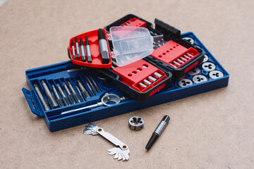 Metal thread cutting tap and die set with handle, drill bits, and gauges arranged on a wooden workbench. Industrial mechanic tools for metalworking, threading, repair and engineering work.