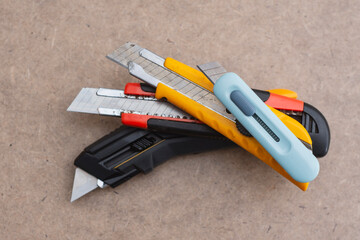 Set of utility knives and box cutters of different colors lying on a wooden surface. Concept of...