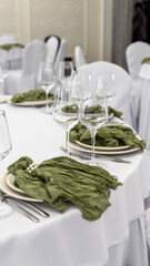 elegant wedding table setting of a round table in white and green tones. glasses, green cloth napkins, white tablecloth, white necklace