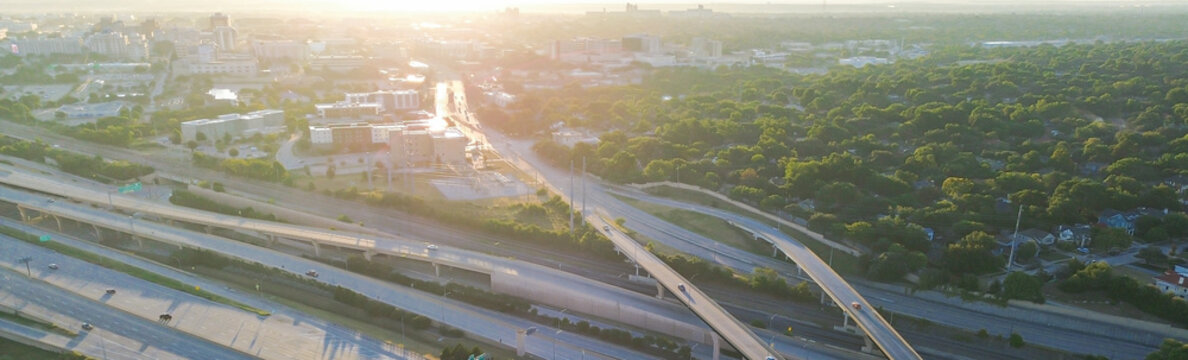 Panorama aerial view modern stacked interchange near Fort Worth Downtown bridge allowing traffic beneath, surrounded by lush tree canopy, directional ramps, skyline access via arterial highway