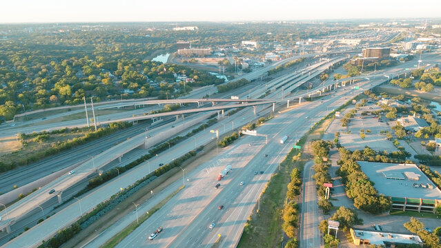 Multilane stacked interchange near Fort Worth Medical District dense tree buffers, flat-roof industrial buildings featuring HVAC units, layered highway ramps leading toward healthcare corridor