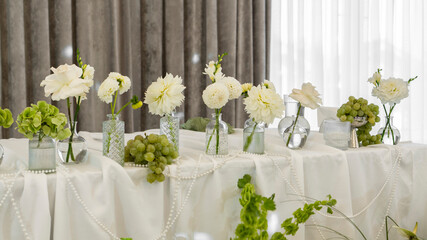 wedding decoration of the bride's table. Flower arrangement in white and green colors, vases with flowers, white tablecloth, necklace. Rose, chrysanthemum, dahlia, grapes, hydrangea, anthurium