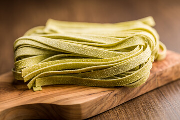 Green tagliatelle pasta on cutting board on wooden table.