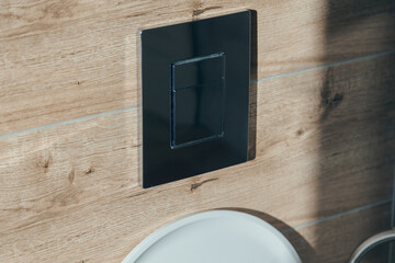 Close-up of a chrome dual flush button on a wall with wood-grain tiles