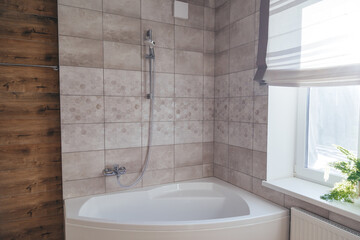 Corner acrylic bathtub with plastic front panel underneath in a bathroom with a window.