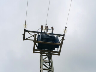 power transformer mounted on utility pole, surrounded by transmission lines under cloudy sky. setup provides electricity to surrounding rural region