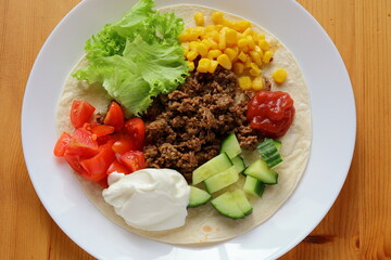 Typical Swedish taco. Bread at plate filled with minced meat, corn, lettuce,  tomato, cucumber. Also red and white sauce. Mexican food.