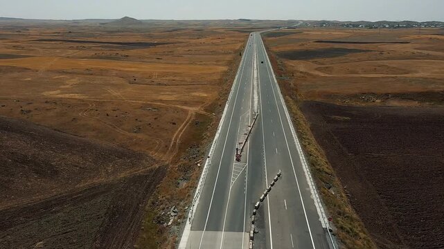 Aerial drone shot of cars driving on a newly constructed highway section through a vast, dry steppe landscape. Infrastructure project, travel, and road repair footage.