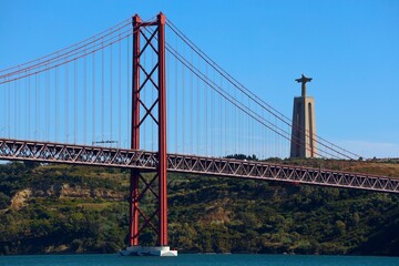 View of famous Lisbon bridge over Tagus river with Jesus Christ statue standing on the hill