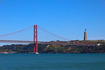View of famous Lisbon bridge over Tagus river with Jesus Christ statue standing on the hill